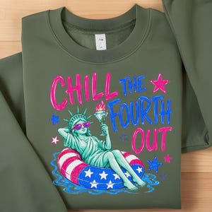 May include: An olive green crewneck sweatshirt featuring a graphic print of the Statue of Liberty wearing pink sunglasses, lounging in a red, white, and blue striped pool float while holding a martini. The text reads CHILL THE FOURTH OUT.