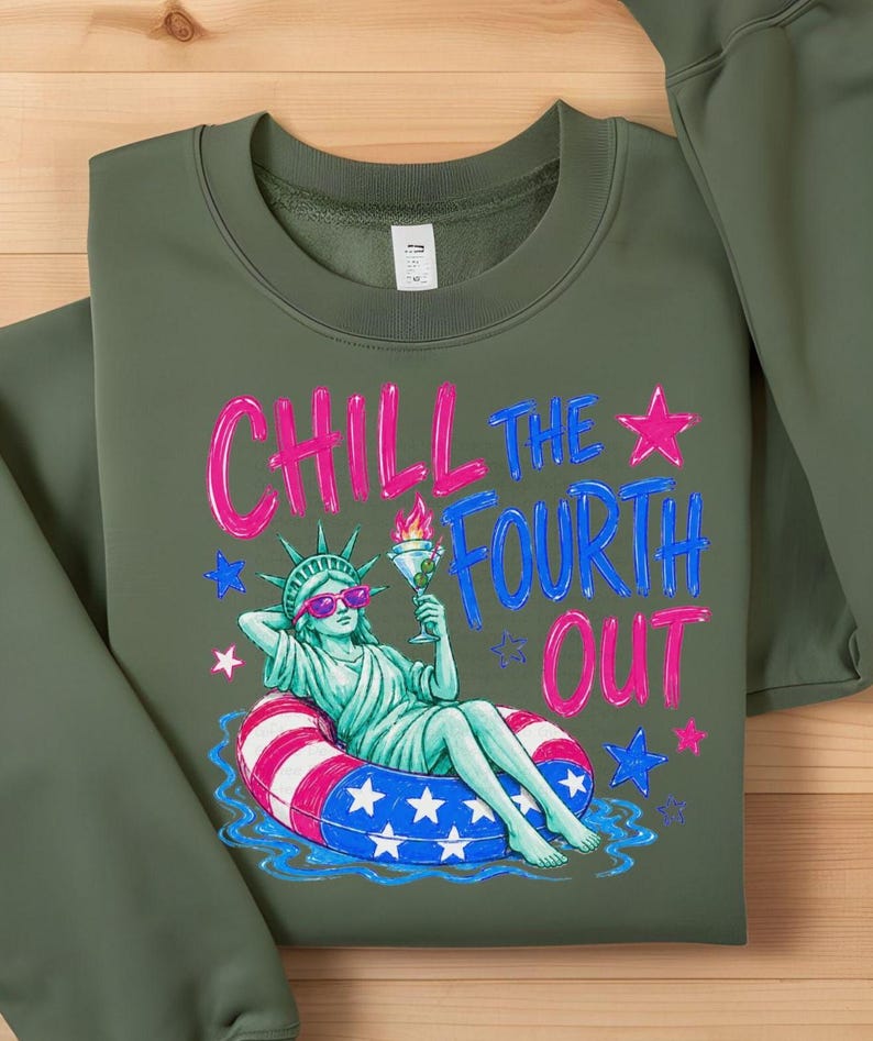May include: An olive green crewneck sweatshirt featuring a graphic print of the Statue of Liberty wearing pink sunglasses, lounging in a red, white, and blue striped pool float while holding a martini. The text reads CHILL THE FOURTH OUT.