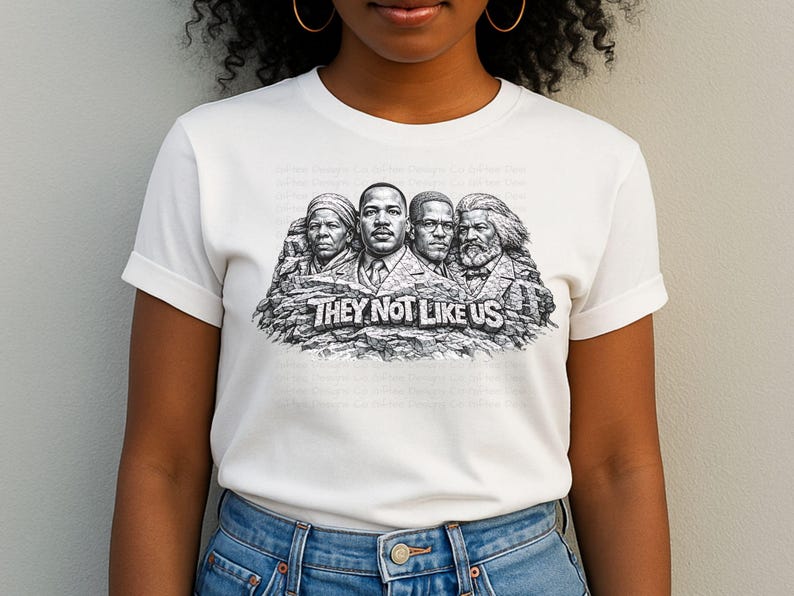 以下が含まれることがあります： 「THEY NOT LIKE US」の文字と、岩に彫られた4人の歴史上の人物の白黒グラフィックが特徴の白いTシャツ。青いジーンズを履いた人が着ています。