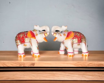 Puede incluir: Dos figuritas de elefante blancas pintadas que se miran. Los elefantes están decorados con pintura roja, dorada y naranja y tienen detalles de joyas.