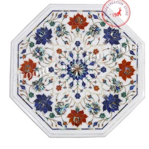 May include: Octagonal white marble table top with intricate floral inlay design. The design features red, blue, and green flowers with mother of pearl accents. The table top is approximately 20 inches in diameter.