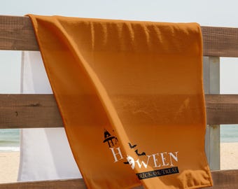 Può includere: Un asciugamano arancione a tema Halloween drappeggiato su una staccionata di legno. L'asciugamano presenta la scritta "HALLOWEEN" con pipistrelli e una grafica di cappello da strega. Sono stampate anche le parole "TRICK OR TREAT".