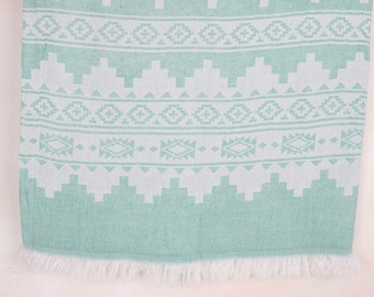 May include: A mint green and white patterned towel with a geometric design. The towel features a repeating pattern of diamonds, triangles, and other shapes. The bottom edge has a white fringe.