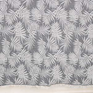May include: A gray and white beach towel with a repeating pattern of tropical palm leaves. The towel has a fringed edge and is made of a soft, absorbent material. The design is a classic, neutral style.