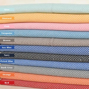 Può includere: Una pila di 12 asciugamani turchi in vari colori, tra cui menta, senape, rosa, turchese, marrone, blu saxe, blu navy, blu petrolio, grigio scuro, arancione e rosso. Gli asciugamani sono tessuti con un motivo a spina di pesce.