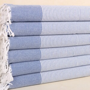 May include: A stack of blue and white striped towels with white fringe. The towels are folded and stacked on a light brown surface.