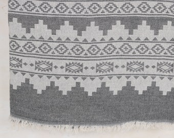 May include: A gray and white patterned textile with a geometric design. The pattern includes diamond, cross, and stepped shapes. The bottom edge has a fringe. The textile is likely a blanket or throw.
