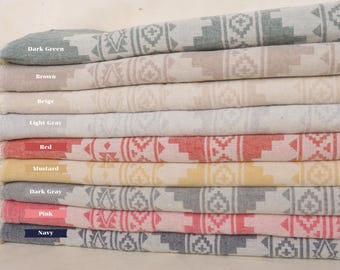 May include: A stack of ten patterned Turkish towels in various colors, including dark green, brown, beige, light gray, red, mustard, dark gray, pink, and navy. The towels have a geometric design and are made of cotton.