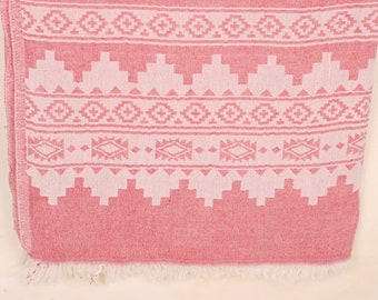 Puede incluir: Textil estampado en rojo y blanco con un diseño geométrico. La tela presenta patrones repetidos de diamantes, triángulos y cuadrados. Los bordes están acabados con flecos.
