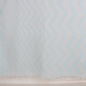 May include: A light blue and white chevron patterned beach towel with a fringed edge. The towel is made of a lightweight fabric, perfect for the beach or pool. The zig-zag design adds a stylish touch.