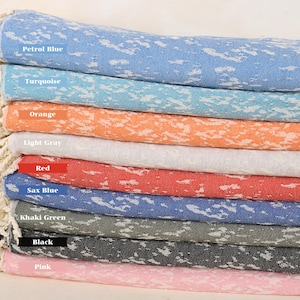 Puede incluir: Una pila de diez toallas turcas en varios colores, incluyendo azul petróleo, turquesa, naranja, gris claro, rojo, azul saxo, verde caqui, negro y rosa. Cada toalla tiene un patrón de salpicaduras blancas.