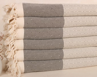May include: A pile of six folded cream-coloured towels featuring a dark grey diamond pattern. Each towel has fringed edges and is neatly stacked, creating a tidy display. These towels are suitable for use in the bathroom or at the beach.