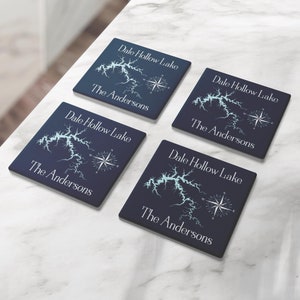 May include: Four blue square coasters with a white outline of a lake and compass design. The text "Dale Hollow Lake" and "The Andersons" is printed on each coaster.