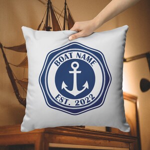 Könnte beinhalten: Ein weißes Kissen mit einem blauen nautischen Ankerdesign. Der Anker befindet sich in einem Kreis mit dem Text "BOAT NAME EST. 2022".