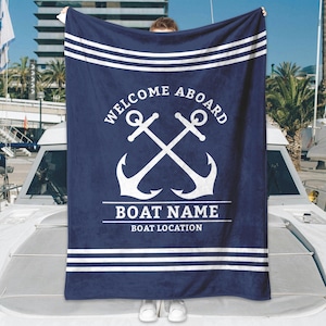 May include: Navy blue blanket with white nautical design. The blanket features the text "WELCOME ABOARD" above crossed anchors. Below the anchors are lines for "BOAT NAME" and "BOAT LOCATION". White stripes border the top and bottom.