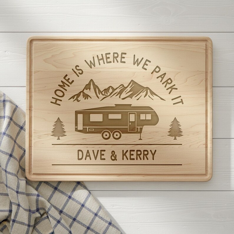 May include: A rectangular wooden cutting board with a carved design. The design includes a camper, mountains, and text that reads "HOME IS WHERE WE PARK IT" and "DAVE & KERRY". Two trees flank the camper.