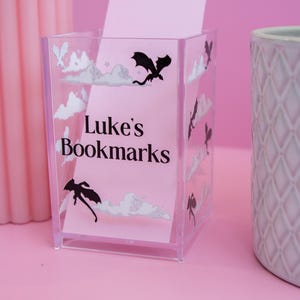 May include: A clear acrylic pencil holder with a dragon design and the text "Luke's Bookmarks".