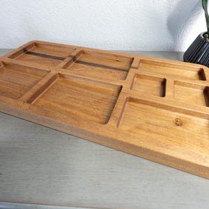 May include: A wooden desk organizer with multiple compartments of varying sizes. The organizer is rectangular with a light brown finish. It has a sloped design and is made of wood. The compartments are designed to hold various office supplies.