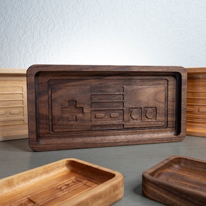 May include: Four wooden trays with a carved video game controller design. The trays are made of different types of wood, including walnut and maple. The trays are all different sizes and shapes.