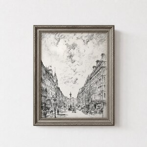 May include: A framed black and white ink sketch depicting a city street scene with tall buildings lining both sides of a wide avenue. A central monument stands in the distance under a cloudy sky, with small figures walking along the street level.