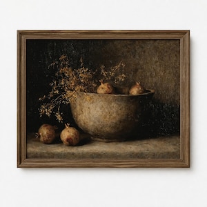 May include: A framed still life painting depicting a large, mottled stone bowl containing dried golden foliage and two pomegranates. Two additional pomegranates rest on the surface beside the bowl, all rendered in muted earth tones and dark shadows.