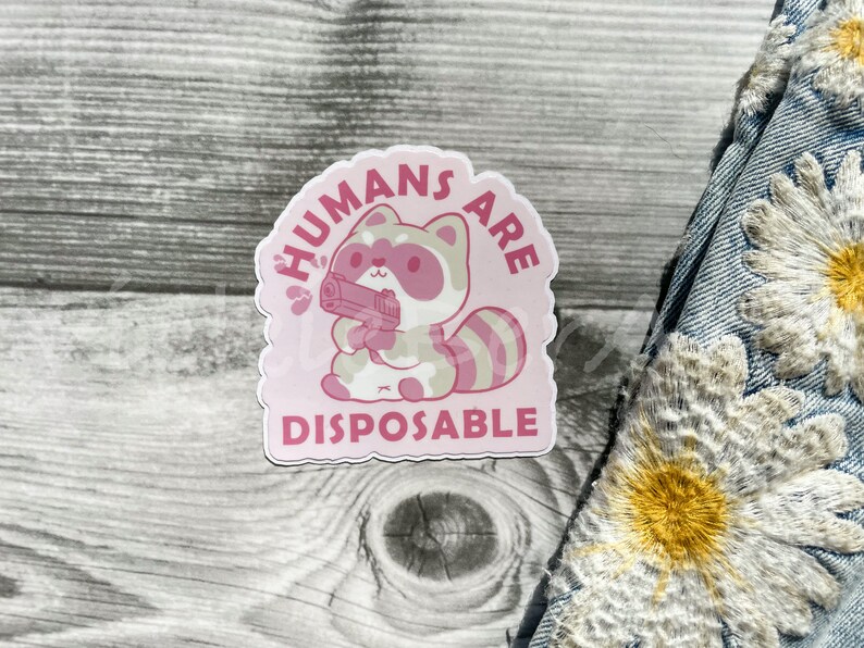 May include: Pink sticker with a cartoon raccoon holding a gun and the text "HUMANS ARE DISPOSABLE".