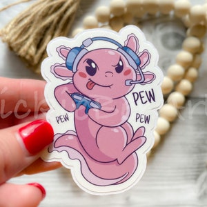 May include: A pink axolotl wearing a blue headset and holding a video game controller. The axolotl has a tongue sticking out and the text "PEW" is written on the sticker three times.