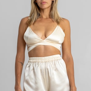 May include: A cream-colored satin top with a wrap-style design and matching satin shorts. The top has a deep V-neckline and adjustable straps.
