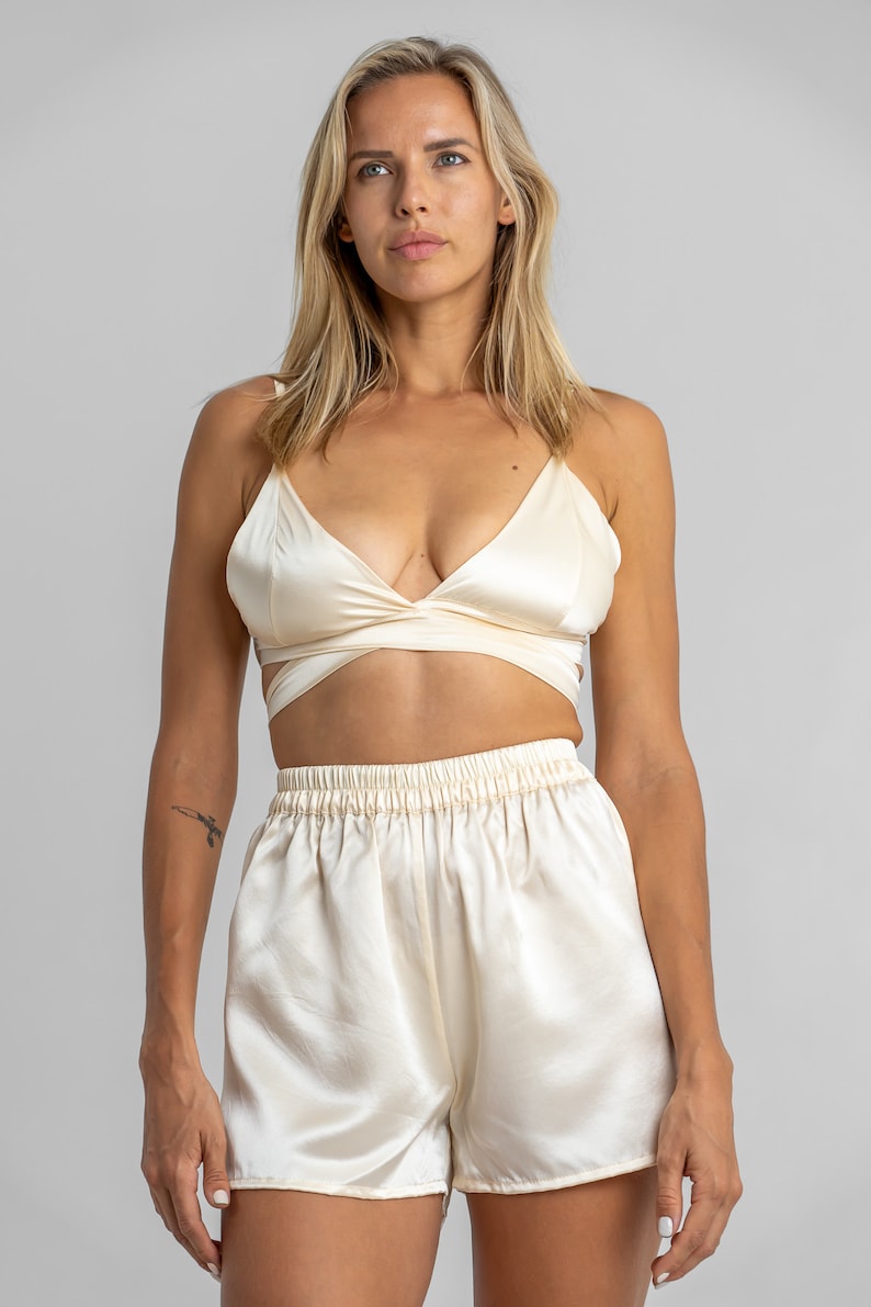 May include: A cream-colored satin top with a wrap-style design and matching satin shorts. The top has a deep V-neckline and adjustable straps.