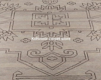 May include: A light beige area rug featuring a dark brown geometric pattern with symmetrical lines, angular shapes, and floral-inspired motifs. The text Kohinoor carpet store is printed in white across the center of the rug's detailed design.