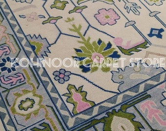 May include: A rectangular area rug with a cream-colored base featuring a geometric floral pattern in shades of light blue, lime green, and soft pink. The rug includes a decorative border and the text KOHINOOR CARPET STORE printed across the center.