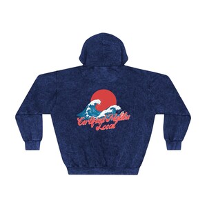 May include: A navy blue hooded sweatshirt with a distressed look. The back of the sweatshirt features a graphic of a red sun rising over blue waves with the text "Certified Malibu Local" in red and white.