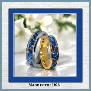 May include: Two wedding rings with a blue and black inlay. One ring is silver, and the other is gold. The rings are set against a soft, blurred background. The text "Haloman Reflections" and "MADE IN THE USA" are visible.