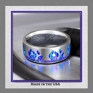 Può includere: Anello argentato con un motivo a fiamma blu e viola. L'anello presenta il testo "Halcyon Reflections" e "MADE IN THE USA". Un gioiello.
