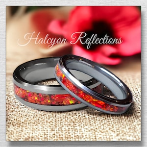 May include: Two silver wedding bands with a red and orange opal inlay. The bands are on a textured fabric surface.