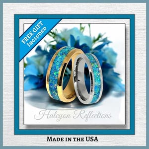 Puede incluir: Dos anillos de boda con incrustaciones de ópalo azul. Un anillo es dorado, el otro plateado. Los anillos están colocados sobre un fondo de flores azules. El texto "Halcyon Reflections" y "MADE IN THE USA" son visibles.