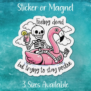 May include: A white sticker or magnet with a pink flamingo pool float and a skeleton holding a glass of lemonade. The text reads "Feeling dead but trying to stay positive".