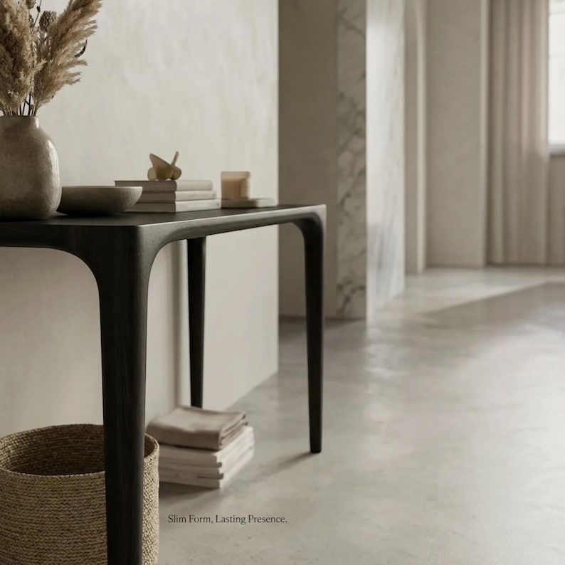 Puede incluir: Una mesa consola de madera oscura con cuatro patas delgadas y una superficie rectangular lisa. Sobre la mesa hay un jarr&oacute;n de cer&aacute;mica con hierbas secas, un cuenco peque&ntilde;o, una pila de libros y una vela. El texto Slim Form, Lasting Presence es visible.
