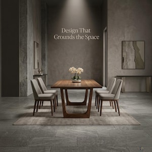 May include: A rectangular wooden dining table with a dark brown finish and U-shaped legs, accompanied by four light gray upholstered chairs. The text "Design That Grounds the Space" is visible on the wall above the table, which holds a white orchid.