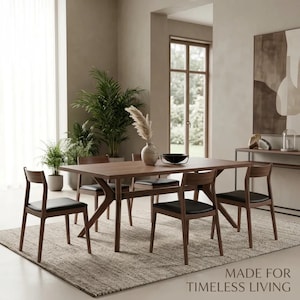 May include: A rectangular wooden dining table with four matching chairs featuring black upholstered seats. The set is arranged on a textured area rug in a room with neutral walls and green potted plants. The text MADE FOR TIMELESS LIVING is visible.