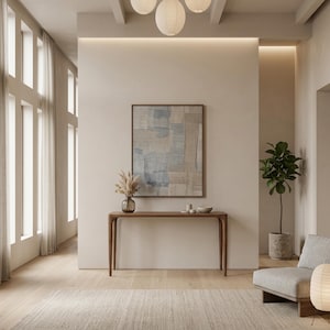 Op de afbeelding: Een moderne woonkamer met een licht kleurenpalet. Het beschikt over een houten console, een abstracte ingelijste kunstwerk, een plant in een pot en een grijze fauteuil. De kamer wordt verlicht door natuurlijk licht van een groot raam en papieren lantaarns.