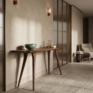 May include: A dark wood console table with four tapered legs and a smooth rectangular top. A round, teal-coloured ceramic bowl sits on the left side of the table, while three small, square, gold-framed glass candle holders are placed on the right.