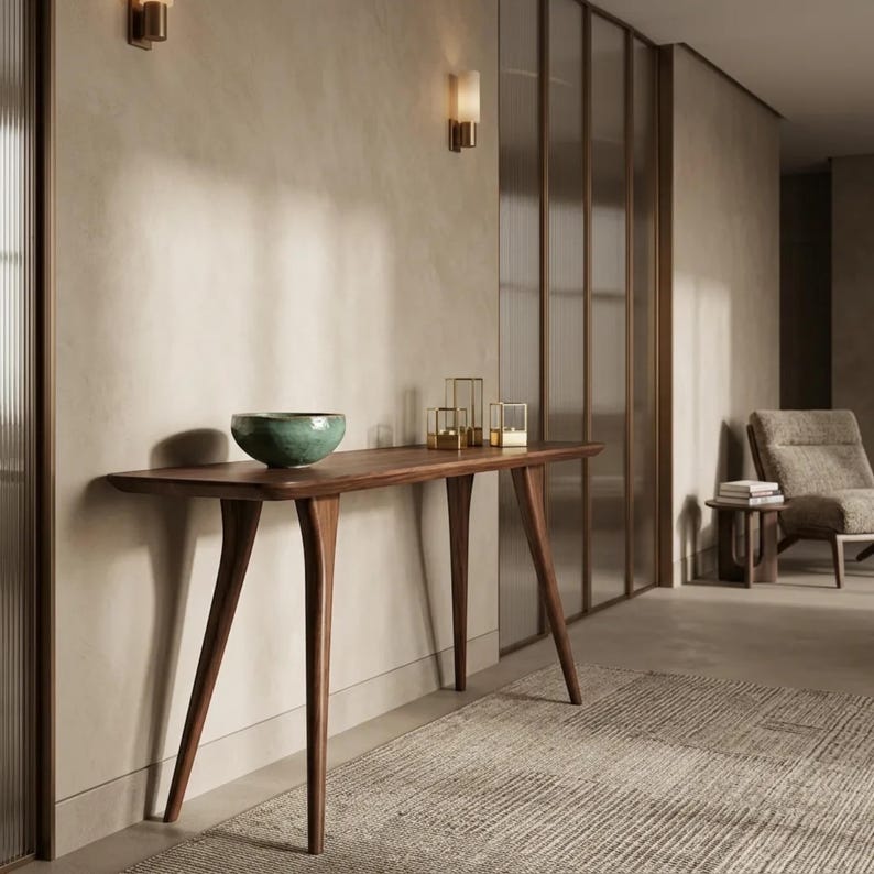 May include: A dark wood console table with four tapered legs and a smooth rectangular top. A round, teal-coloured ceramic bowl sits on the left side of the table, while three small, square, gold-framed glass candle holders are placed on the right.