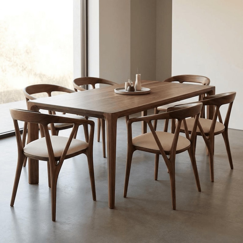 May include: A rectangular wooden dining table with six matching chairs featuring curved backrests and light beige upholstered seats. The table surface is smooth and dark brown, and a small circular tray with two small vases sits in the center.