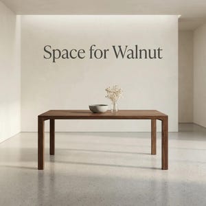 May include: A rectangular dark brown wooden dining table with four straight legs. On the table sits a small grey bowl and a clear glass vase containing white dried flowers. The wall behind the table features the dark text Space for Walnut.