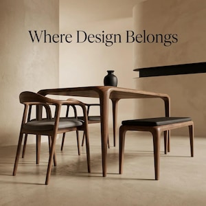 Può includere: Un set da pranzo in legno scuro composto da un tavolo, due sedie con sedute imbottite grigie e una panca con seduta nera. Un vaso nero è posizionato sul tavolo. Il testo "Where Design Belongs" è centrato sopra i mobili in un carattere serif.