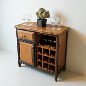Könnte beinhalten: Ein Weinschrank aus Holz mit Schublade, Tür und Weinregal. Der Schrank hat eine natürliche Holzoberfläche mit einem dunklen Metallrahmen. Mehrere Weingläser und eine dekorative Pflanze stehen oben.