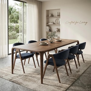 Puede incluir: Una mesa de comedor rectangular de madera con bordes redondeados y seis sillas a juego con asientos y respaldos tapizados en azul oscuro. La pared muestra el texto Crafted for Living. Los muebles se sitúan sobre una alfombra de tonos neutros.
