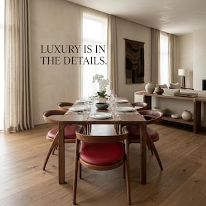 May include: A wooden dining table set with six chairs featuring red leather seats, arranged in a room with light-coloured walls and hardwood floors. The text LUXURY IS IN THE DETAILS is printed on the wall above the table, which is set with white plates.