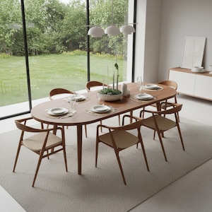 May include: A modern dining room set featuring a large oval wooden table with six matching chairs. The chairs have light-colored seats and curved wooden frames. The table is set with plates, silverware, and glassware. A white rug and a large window are also visible.